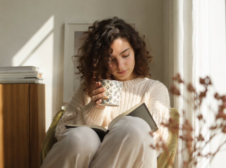mujer leyendo tranquila en casa con una taza, representando el autocuidado y el egoísmo sano